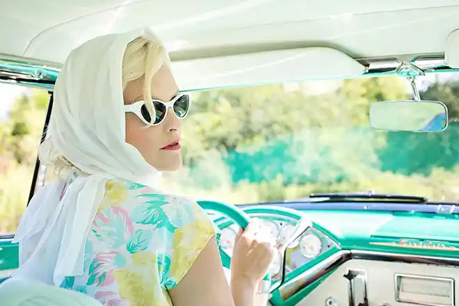 Woman with white vail over head and sitting in classic sixties car